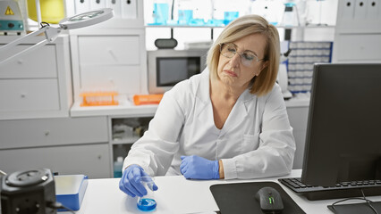 A focused middle-aged woman scientist analyzing a sample in a laboratory setting, surrounded by equipment and a computer.