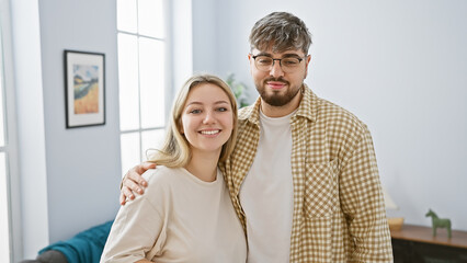 Smiling woman and bearded man embracing warmly in a cozy, bright living room.