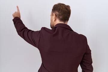 Middle age business man with beard wearing suit and tie posing backwards pointing ahead with finger hand