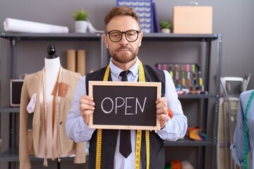 Middle age man with beard dressmaker designer holding open sign thinking attitude and sober...