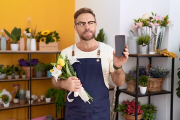 Middle age man with beard working at florist shop showing smartphone screen smiling looking to the...
