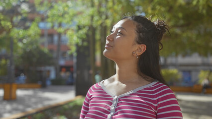 A contemplative young hispanic woman enjoys a serene moment outdoors in a lush city park.