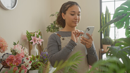 Hispanic woman using smartphone in flower shop with plants and floral arrangement background
