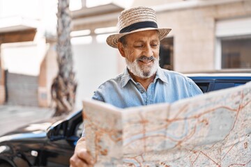 Senior grey-haired man tourist holding city map standing by car at street