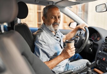 Senior grey-haired man drinking coffee sitting on car at street