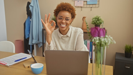 Smiling african american woman giving ok sign in a home office setup with laptop and decor
