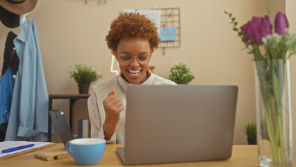 Joyful african american woman using a laptop in a well-decorated home office space.