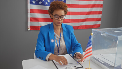 An african american woman wearing a badge sits pensively at a voting station, with the us flag in...