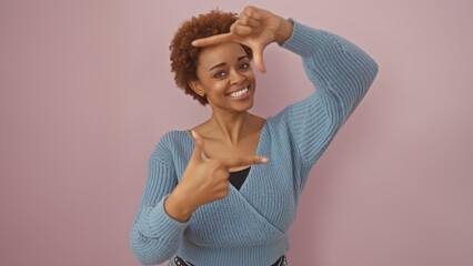 Smiling african american woman making a frame with her hands against a pink background, symbolizing...