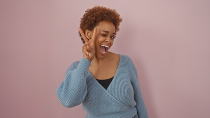 An african american woman shows joy with a playful peace sign against a pink background.