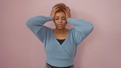 A stressed african american woman with hands on head against a pink background, portraying worry or...