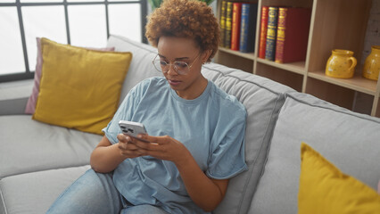An attractive african american woman using a smartphone while relaxing on a comfortable couch...