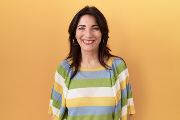 Middle age hispanic woman standing over yellow background with a happy and cool smile on face....