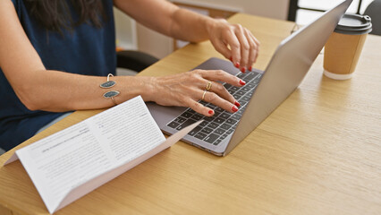Professional woman typing on a laptop in an office with a coffee cup and documents, depicting a...