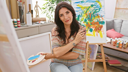 Mature hispanic woman artist painting in a bright studio interior, showcasing creativity and fine...