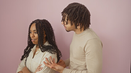 A man and a woman, dressed casually, are posing together against a solid pink background, evoking a...