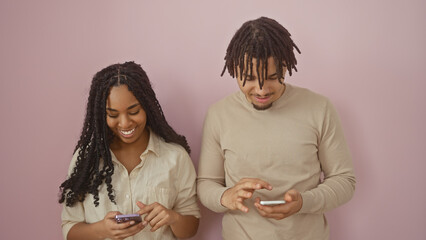 A man and woman enjoy sharing content on their smartphones, standing before a plain pink...