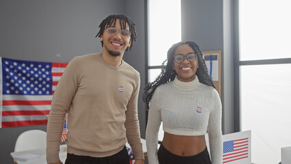 A smiling man and woman with 'i voted' stickers in a room with an american flag