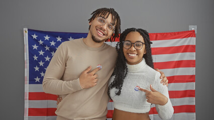 Smiling couple proudly showing 'i voted' stickers with an american flag in an office setting
