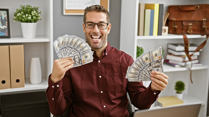 A cheerful hispanic man in an office holding and showing us dollars with a beaming smile