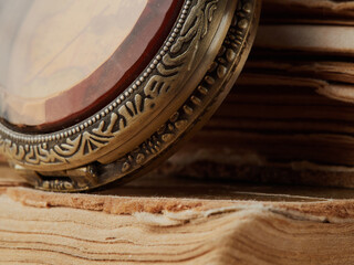 Old clock hanging on a chain on background of old books. Retro clock as a symbol of time a books are a symbol of knowledge. Concept on the theme of history, nostalgia, culture, vintage, antique.