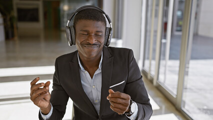 African american man enjoying music in headphones at an office setting, showcasing joy and...