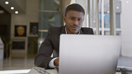 Focused african man working on a laptop in a modern office, portraying professionalism and...