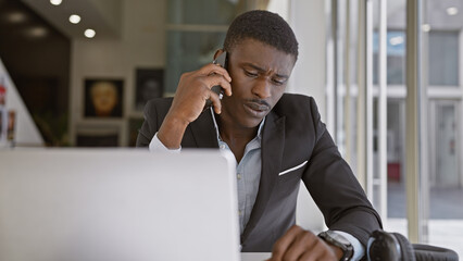 Concentrated african man in business attire working and talking on the phone in an office setting.