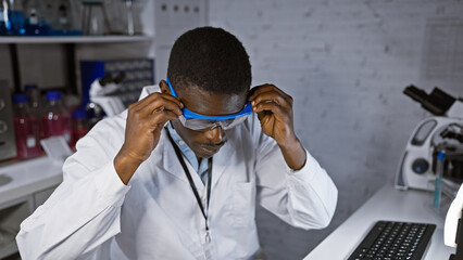 African man wearing labcoat and protective goggles in a science laboratory adjusting equipment.