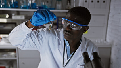 African man in lab coat examining test tube in a laboratory setting, portraying medical or scientific research.