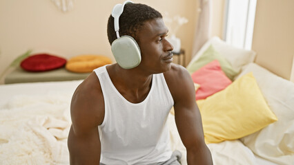 African american man in white tank top relaxing with headphones in a cozy bedroom