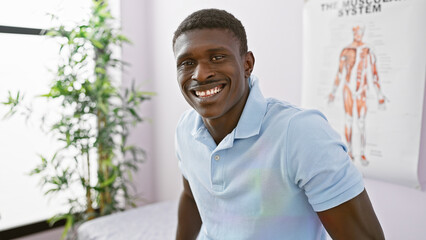 Handsome black man smiling in a clinic with an anatomical poster on the wall.