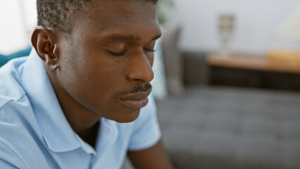 Pensive african man indoors wearing a casual blue shirt with a blurred living room background.