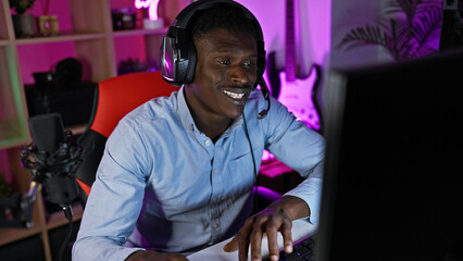 An african american man engaged in gaming with headphones in a colorful illuminated room at night.