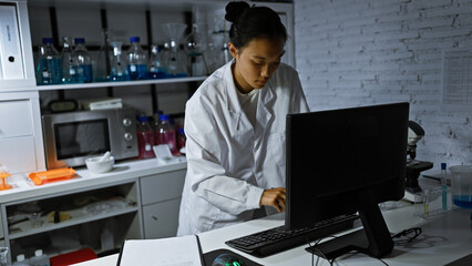 Focused chinese woman scientist using computer in a dimly lit laboratory setting, showcases...