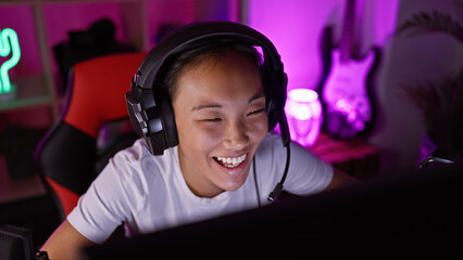 A joyful asian woman wearing headphones enjoys gaming in a vibrant, neon-lit room at night.