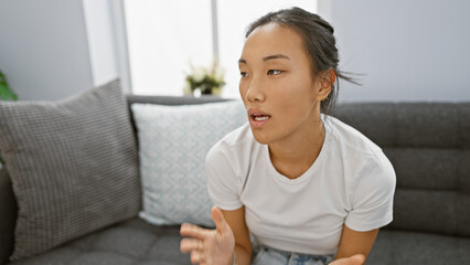 A young asian woman conversing casually in a modern living room, exuding a relaxed, homely...