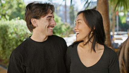 Obraz premium Interracial couple smiling together in a sunny park, portraying love and happiness with a man and woman outdoors.