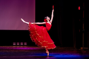 ballerina in a red dress performs a variation from the ballet Don Quixote on the theater stage.