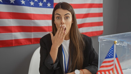 Surprised young hispanic woman indoors with american flag, for themes of election, education, ethnicity, and emotion.