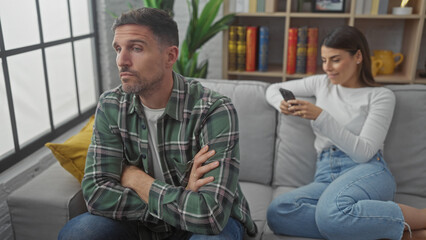 Upset man and woman using smartphone separately, highlighting relationship issues in a living room...