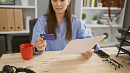 A young woman examines a document in a modern office while holding a credit card.