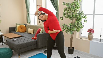 A young woman exercises indoors, bending while listening to music, in a cozy home environment with...