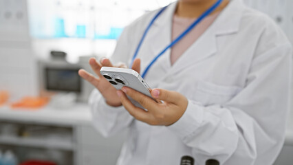 Young hispanic female healthcare professional using a smartphone in a laboratory setting.