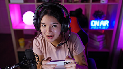 A young hispanic woman plays video games in a vibrant, neon-lit gaming room at night.