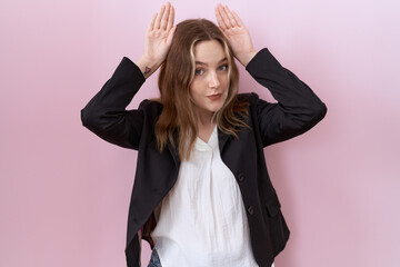 Young caucasian business woman wearing black jacket doing bunny ears gesture with hands palms...