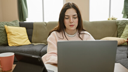 Naklejka premium Focused young woman using laptop in a cozy living room interior