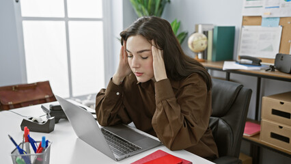 A stressed young caucasian woman experiencing a headache while working on a laptop in a modern...