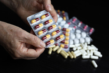 Pills in wrinkled hands of elderly woman on scattered drugs background. Medication in capsules,...