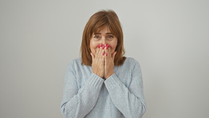 Surprised middle-aged woman in blue sweater covering mouth with hands against a white background
